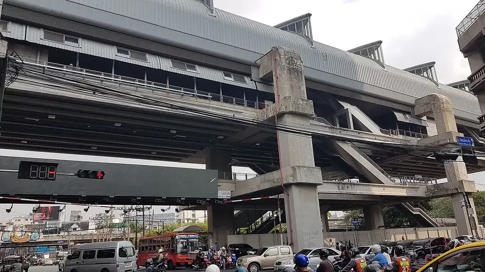 The elevated Airport Rail Link station at Ratchaprarop seen from the junction below, with a bus, vans and motorbikes waiting at a red light