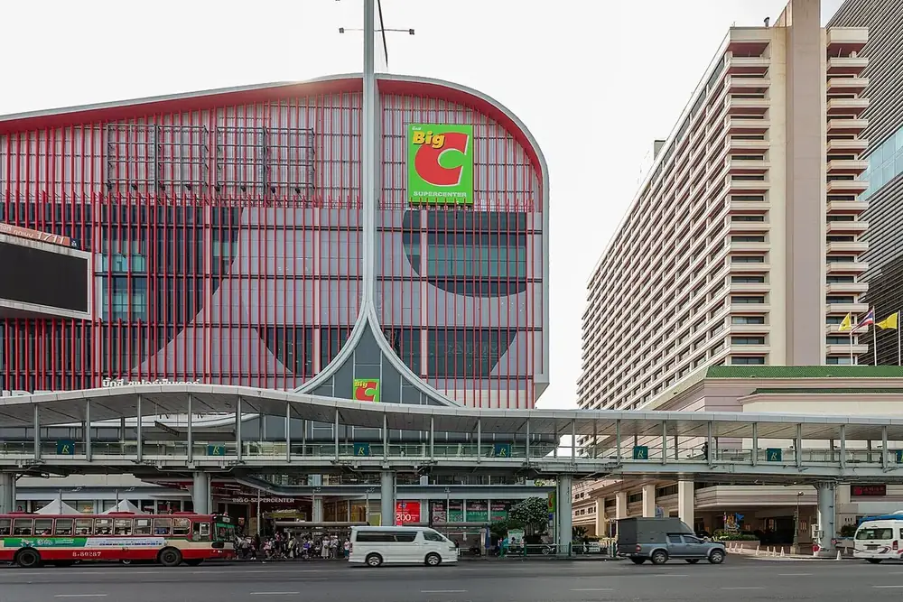 The red-and-white front of Big C Supercenter Ratchadamri behind a raised pedestrian walkway, a city bus on the road below