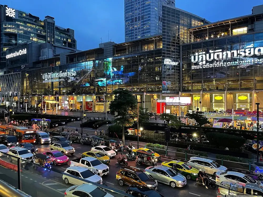CentralWorld in Bangkok at dusk, its lit glass frontage above a road busy with taxis, buses and tuk-tuks